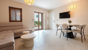A modern living room with a sofa, a round table, and chairs, a television mounted on the wall, and a door leading outside. - Villa Merkur -apartment 1 (Makarska)