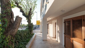 A corridor with a tree, a sign, and a building with wooden shutters. - Villa Merkur -apartment 1 (Makarska)