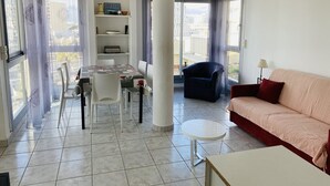 Ein Wohnzimmer mit einer Couch, einem Esstisch mit Stühlen, einem kleinen runden Tisch und einem Bücherregal.