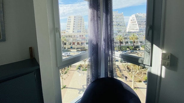 Blick durch ein Fenster mit Vorhängen, der auf eine Straße und Gebäude zeigt.