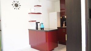 A compact kitchen with a red island, white cabinets, and a clock on the wall. - Apartment with pool and parking - 4 guests (La Grande-Motte)