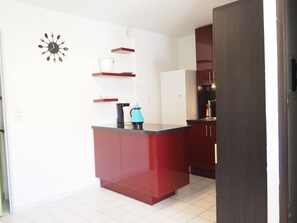 Eine kompakte Küche mit einer roten Kochinsel, weißen Schränken und einer Uhr an der Wand.