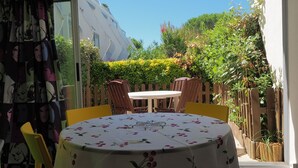 A patio with a table and chairs, a wooden fence, and greenery. - Apartment with pool and parking - 4 guests (La Grande-Motte)