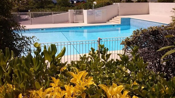 A swimming pool with a modern architectural background, surrounded by greenery and a metal fence. - Apartment with pool and parking - 4 guests (La Grande-Motte)