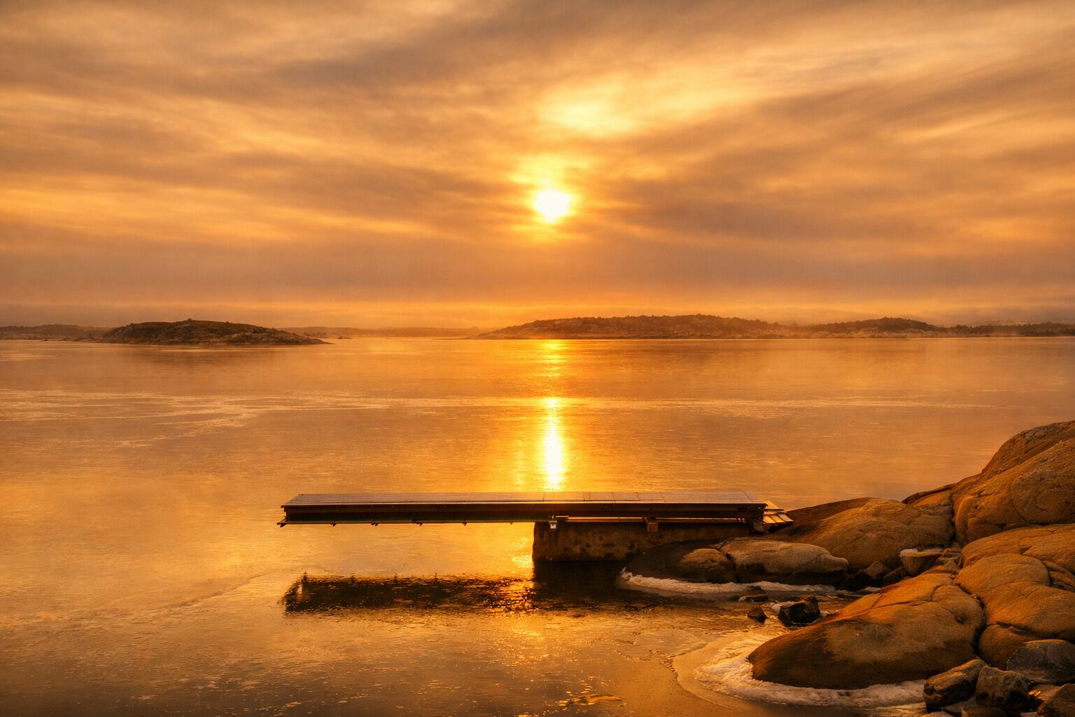 A sunset over a calm body of water with a dock extending into the water.