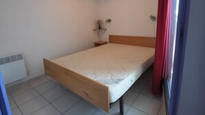 A bedroom with a single bed, a bedside table, a wall-mounted shelf, and a ceiling light fixture. - Apartment near the beach - 4 guests (Le Grau-du-Roi)