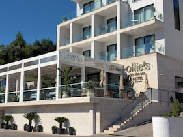 A hotel with a restaurant named 'LUMMA' and 'ollie's' on the ground floor, featuring outdoor seating and a staircase leading to the upper floors.