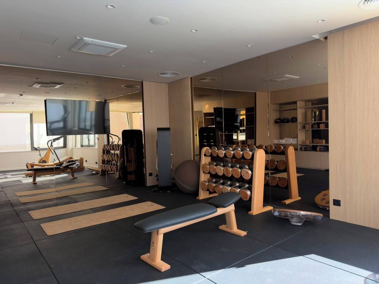 Un gimnasio con equipo de ejercicio, una banca y un muro espejado.
