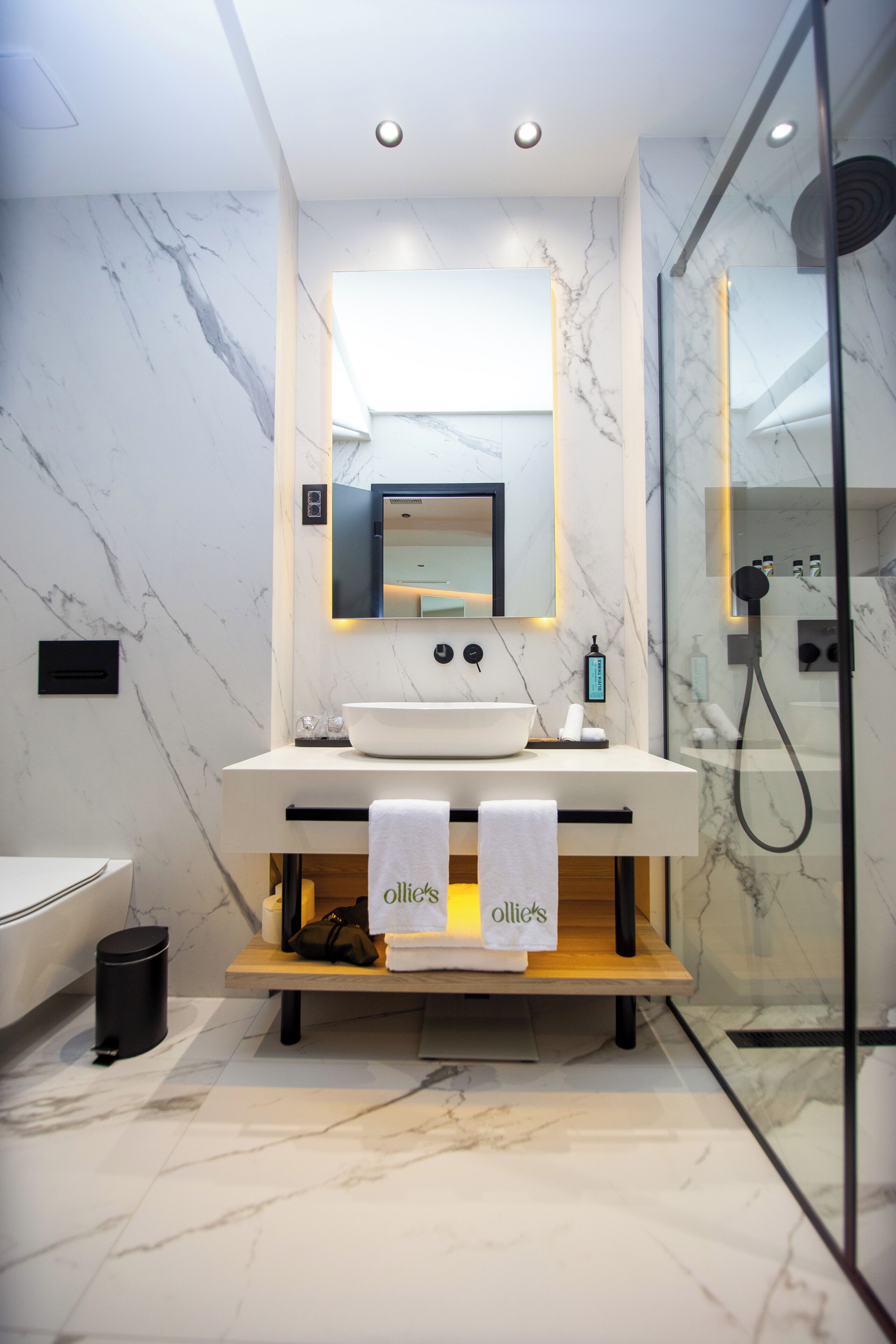 Un baño moderno con lavamanos de mármol, un espejo grande y una ducha con mampara de vidrio.