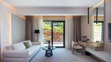 Ein modernes Hotelzimmer mit einer Couch, einem runden Tisch, einem Schreibtisch mit Spiegel und Blick durch eine Glastür.