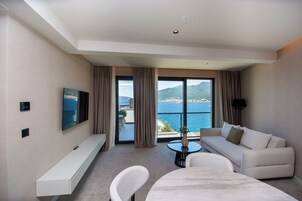 A modern hotel room with a large window, a sofa, a dining table, and a TV.