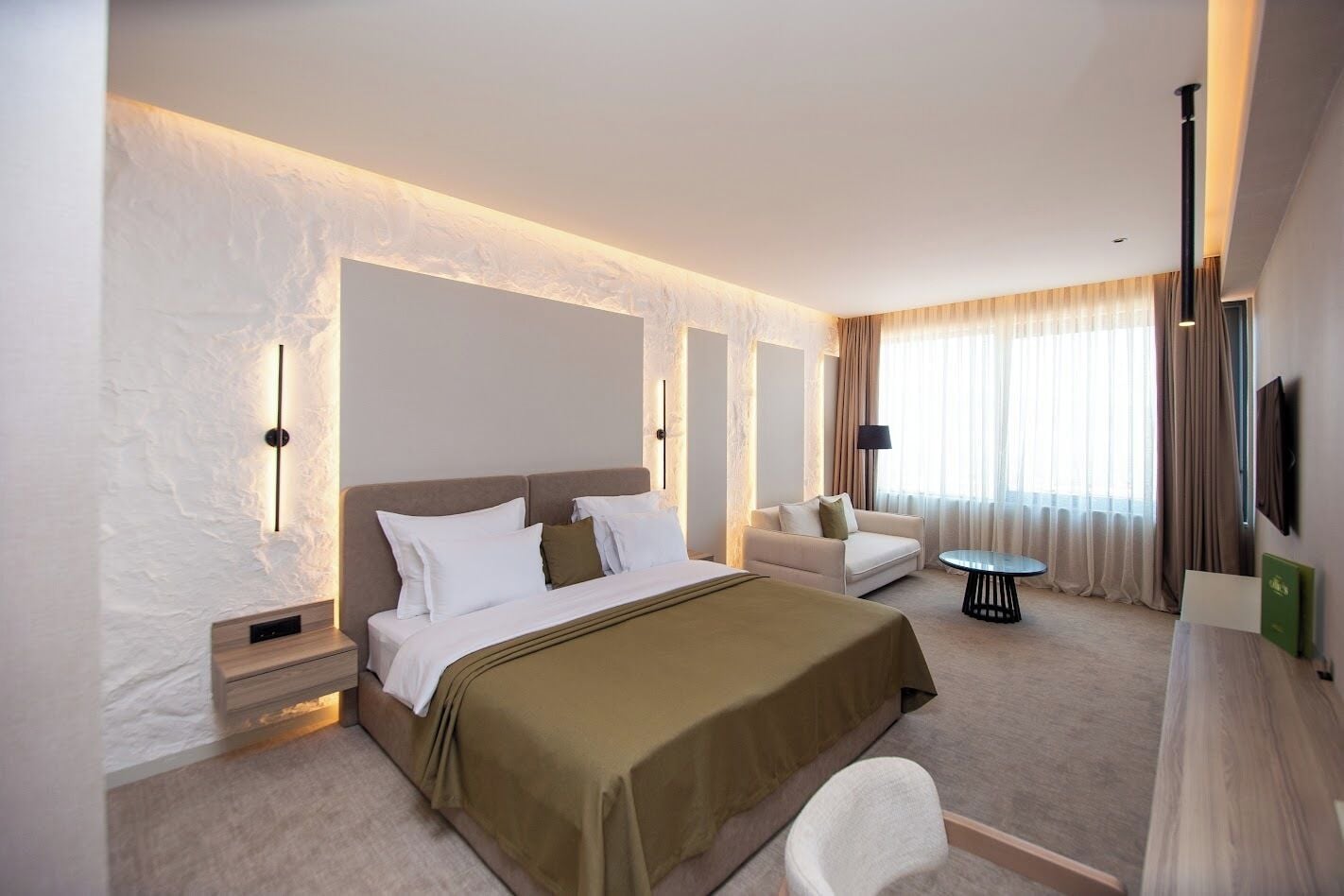 Habitación de hotel con una cama grande, un sofá, una mesita y un televisor.
