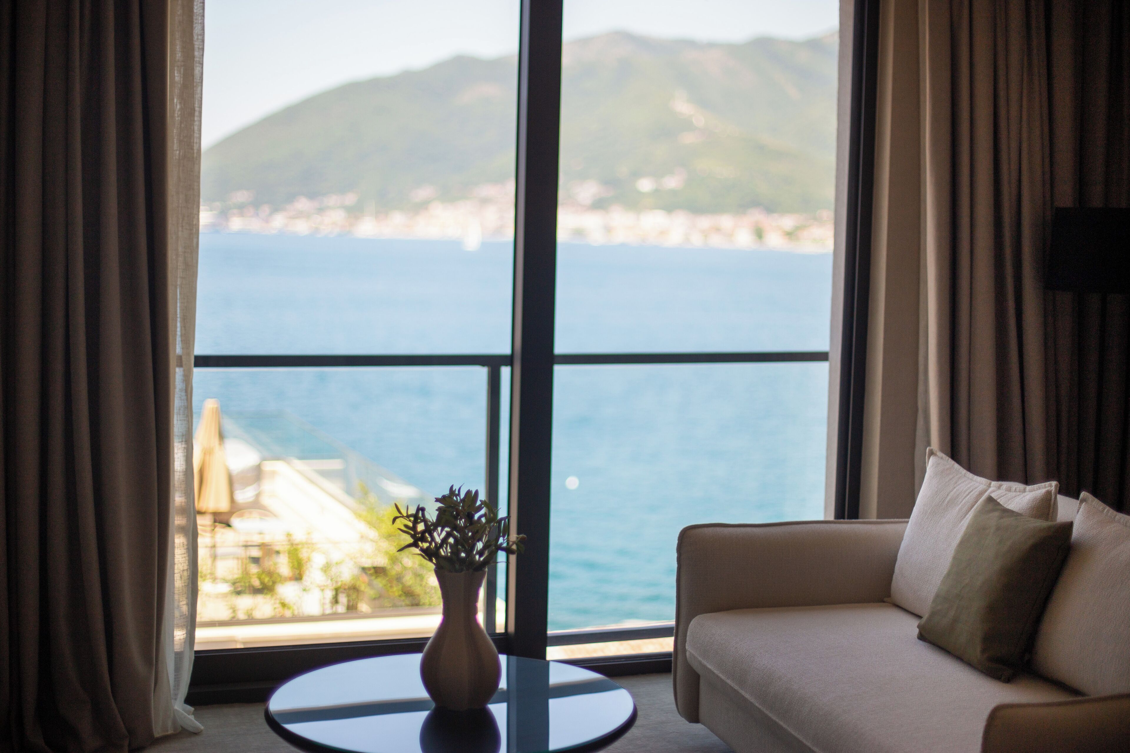 Una habitación con vista al mar, un sofá, una mesita con un jarrón y cortinas.