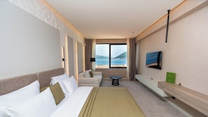 Une chambre d’hôtel avec un lit, un canapé, une petite table ronde, une télévision et une vue sur la mer.