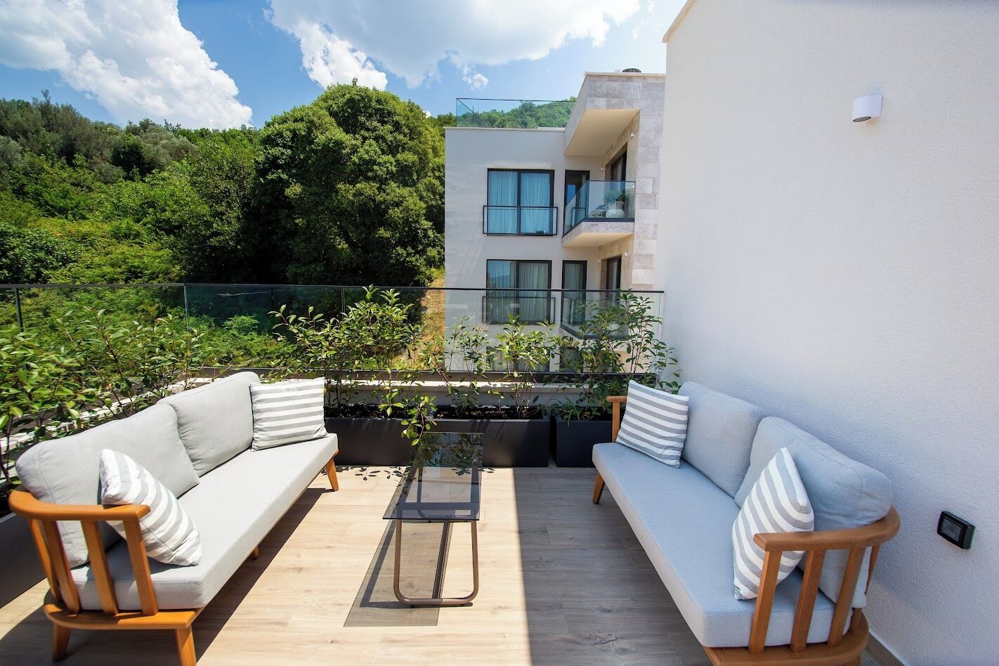A modern outdoor living space with a sofa set, a glass table, and a view of a multi-story building.