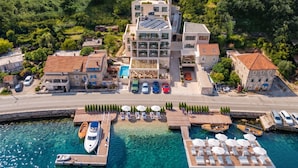 Vue aérienne d’un hôtel situé sur la côte, composé de plusieurs bâtiments, avec un port de plaisance rempli de bateaux et des eaux turquoise d’une clarté exceptionnelle.