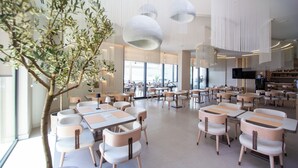 Un vaste espace intérieur doté de nombreuses tables et chaises, de grandes fenêtres et de luminaires suspendus.