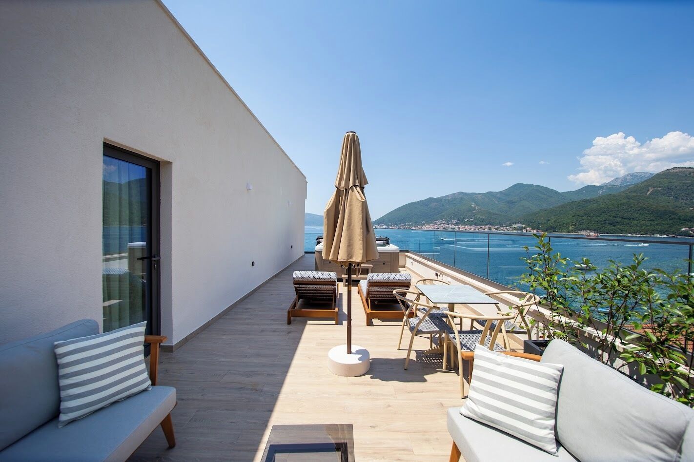 Un balcón con vista al mar, mobiliario de madera y puerta de cristal.
