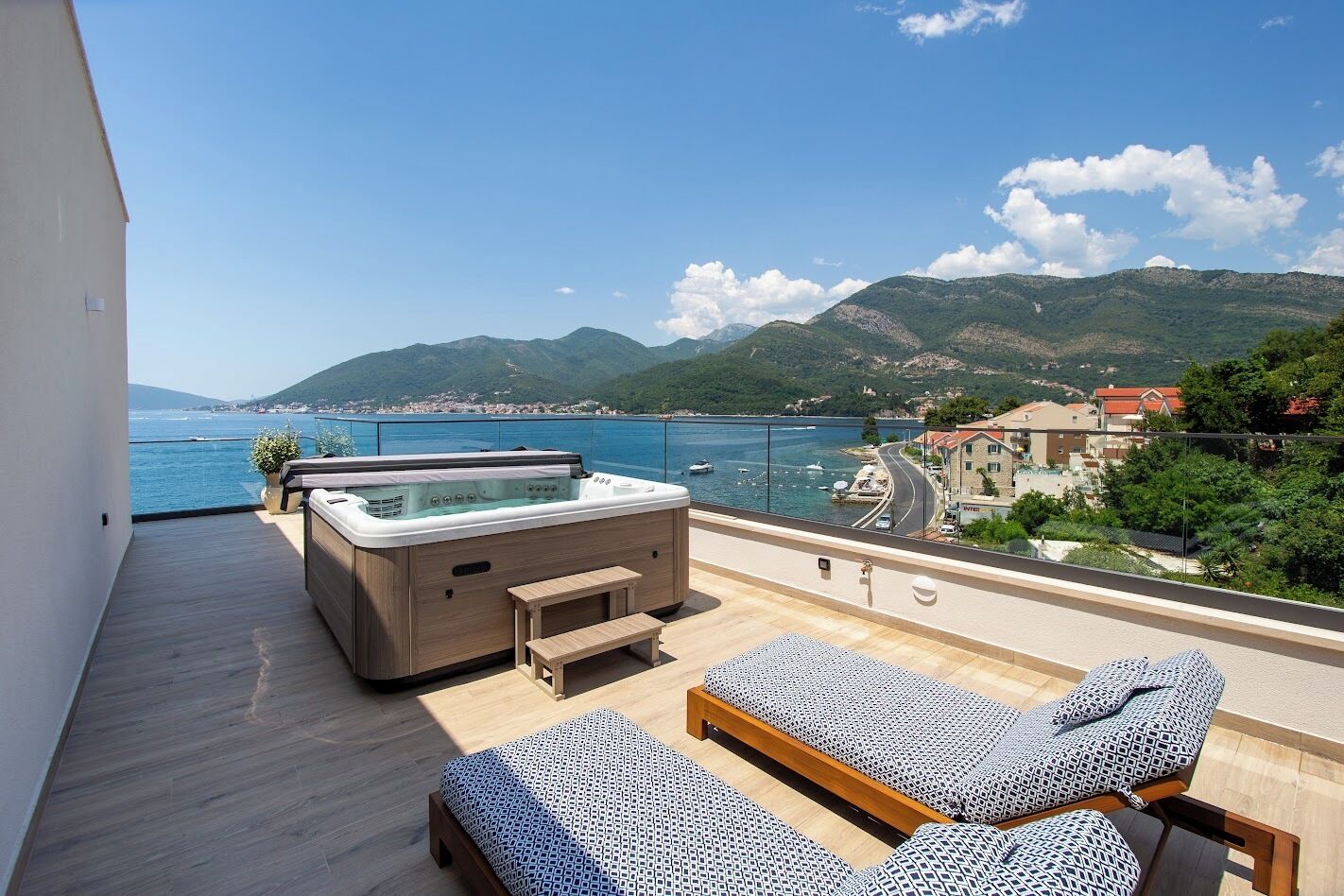 A balcony with a hot tub, lounge chairs, and a view of the sea and mountains.