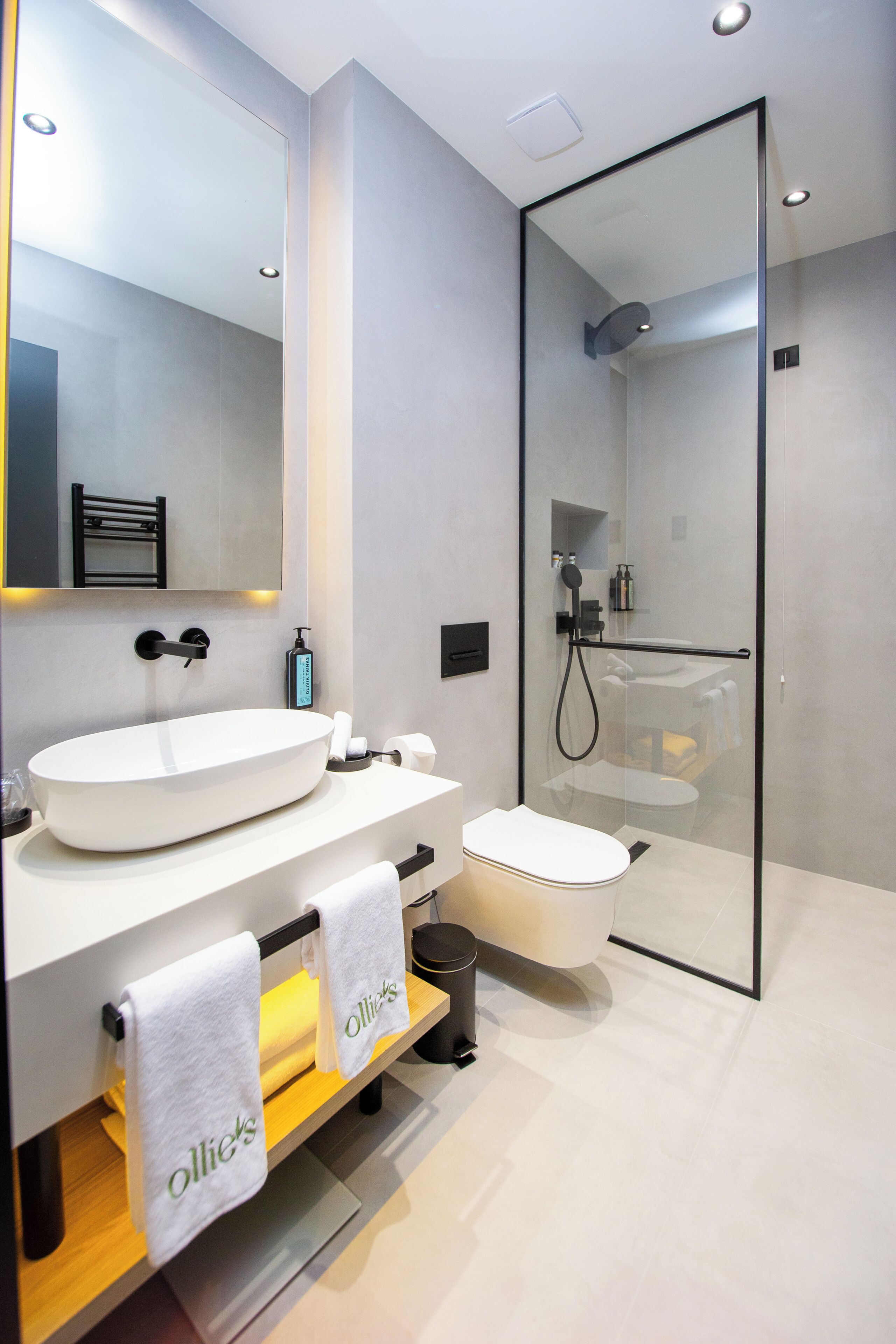 A modern bathroom with a large mirror, a white sink, a toilet, and a glass-enclosed shower.