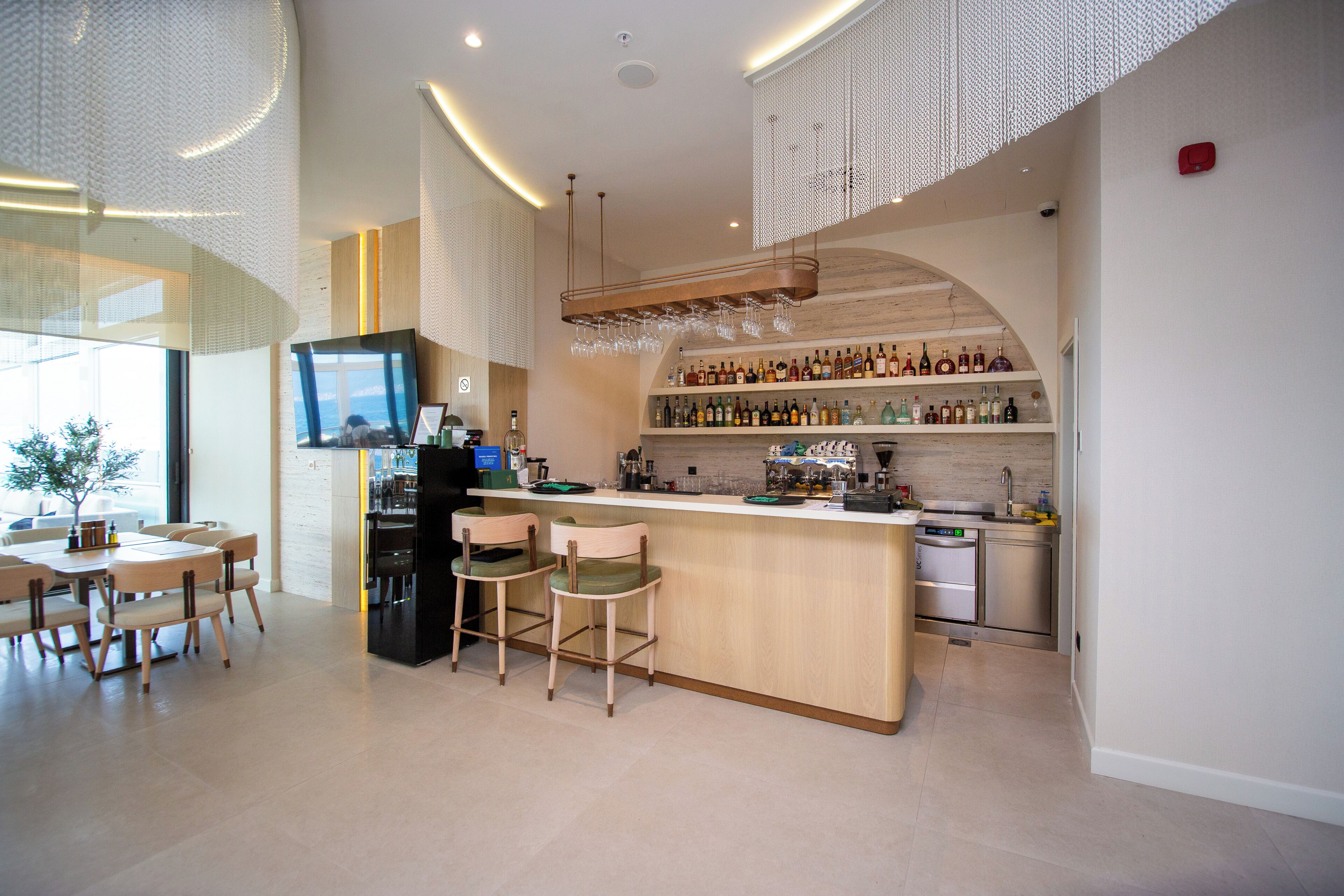 Una cocina moderna con barra, taburetes de madera y una variedad de botellas en estantes.
