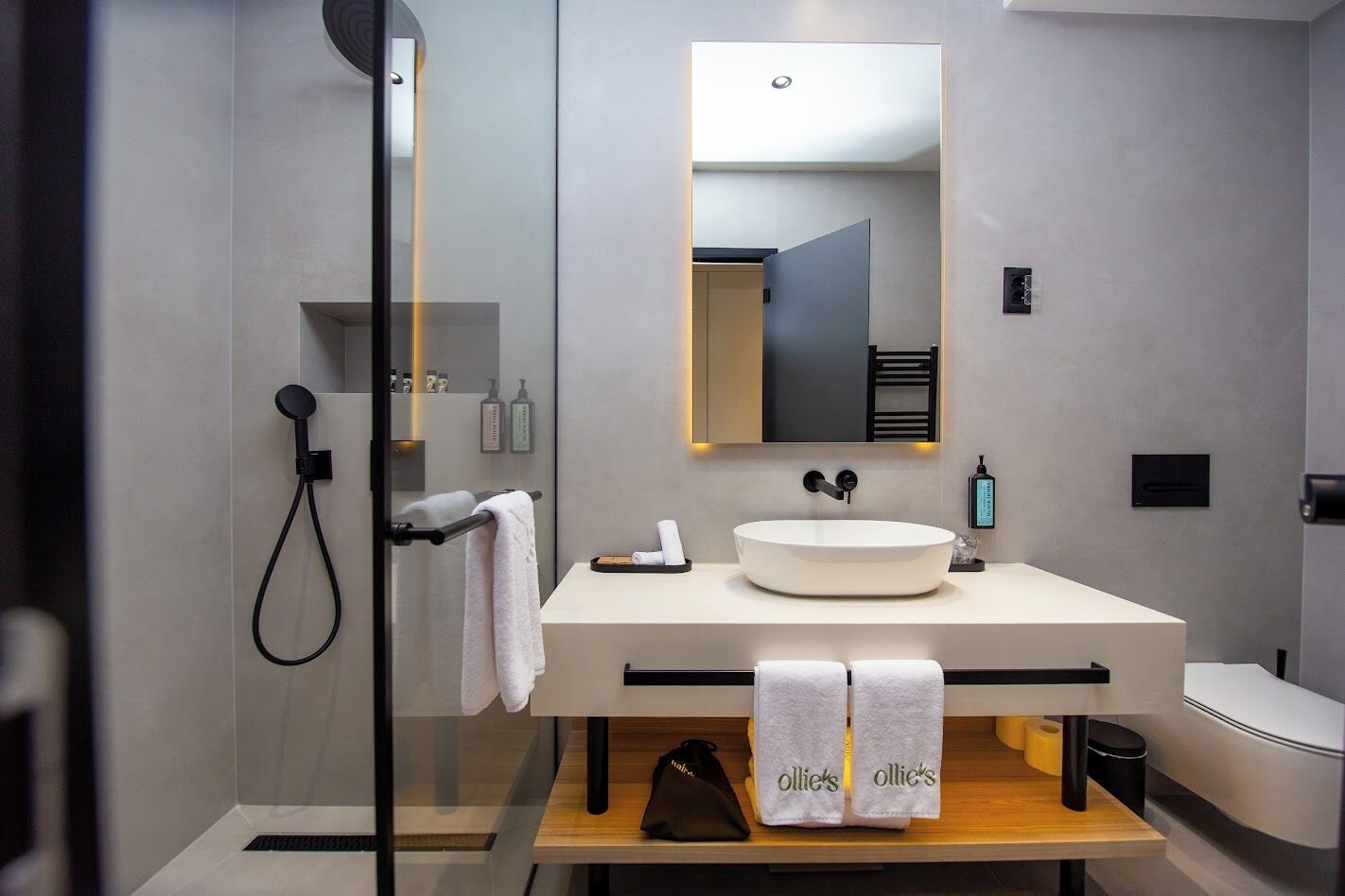 Un baño moderno con ducha envuelta en cristal, un lavabo redondo y un espejo grande.