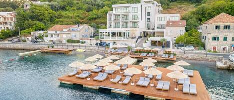 A waterfront property with a wooden deck, lounge chairs, and umbrellas.
