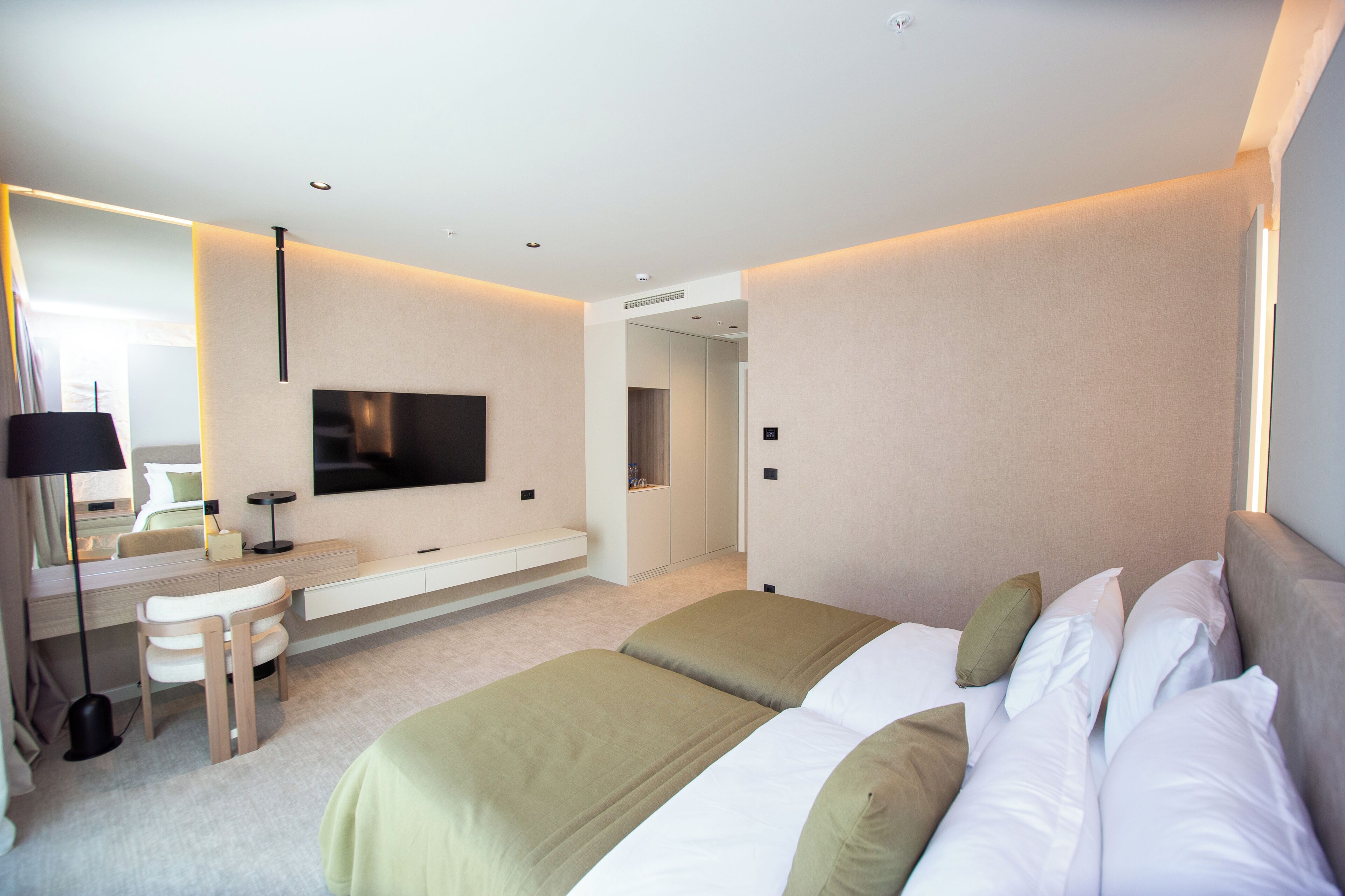 Moderni hotellihuone, jossa on suuri sänky, työpöytä tuolilla, taulutelevisio ja erillinen vaatehuone.