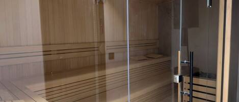 A sauna room with wooden paneling, a glass door, and a wooden bench.
