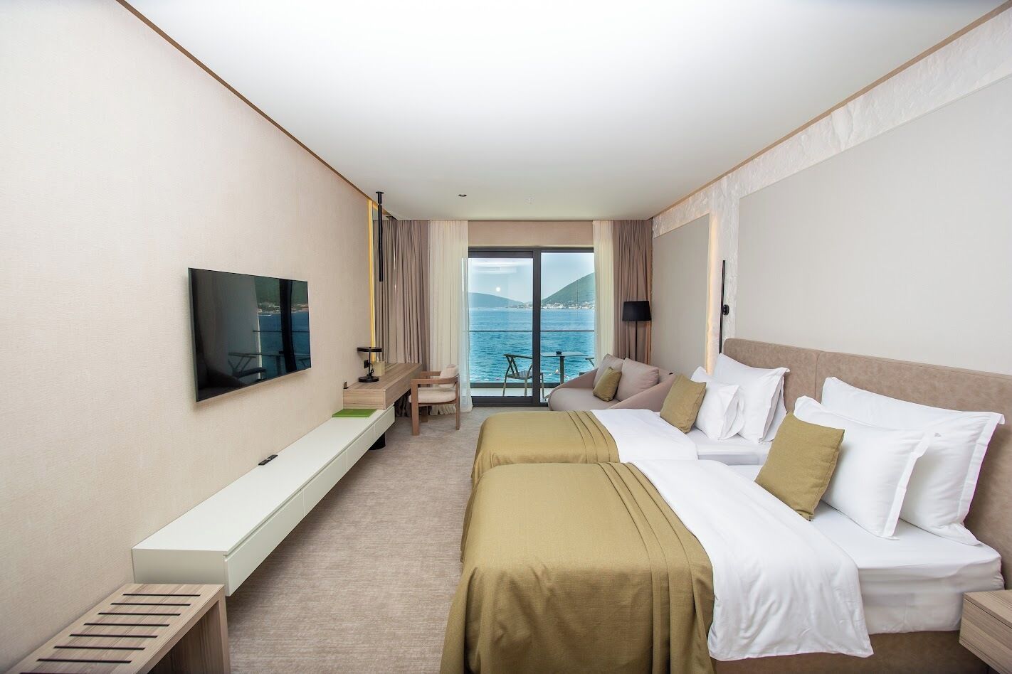 Quarto de hotel com cama, televisão, escrivaninha e vista para o mar.