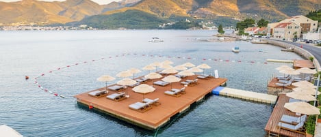 A waterfront resort with a wooden dock, sun loungers, and umbrellas.