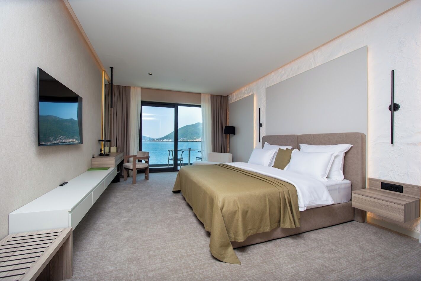 Habitación de hotel con cama, escritorio, silla, televisor y vista al mar.