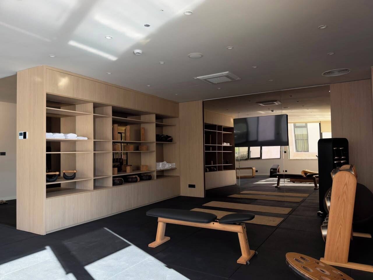 A modern gym with wooden lockers, a bench, and a television.