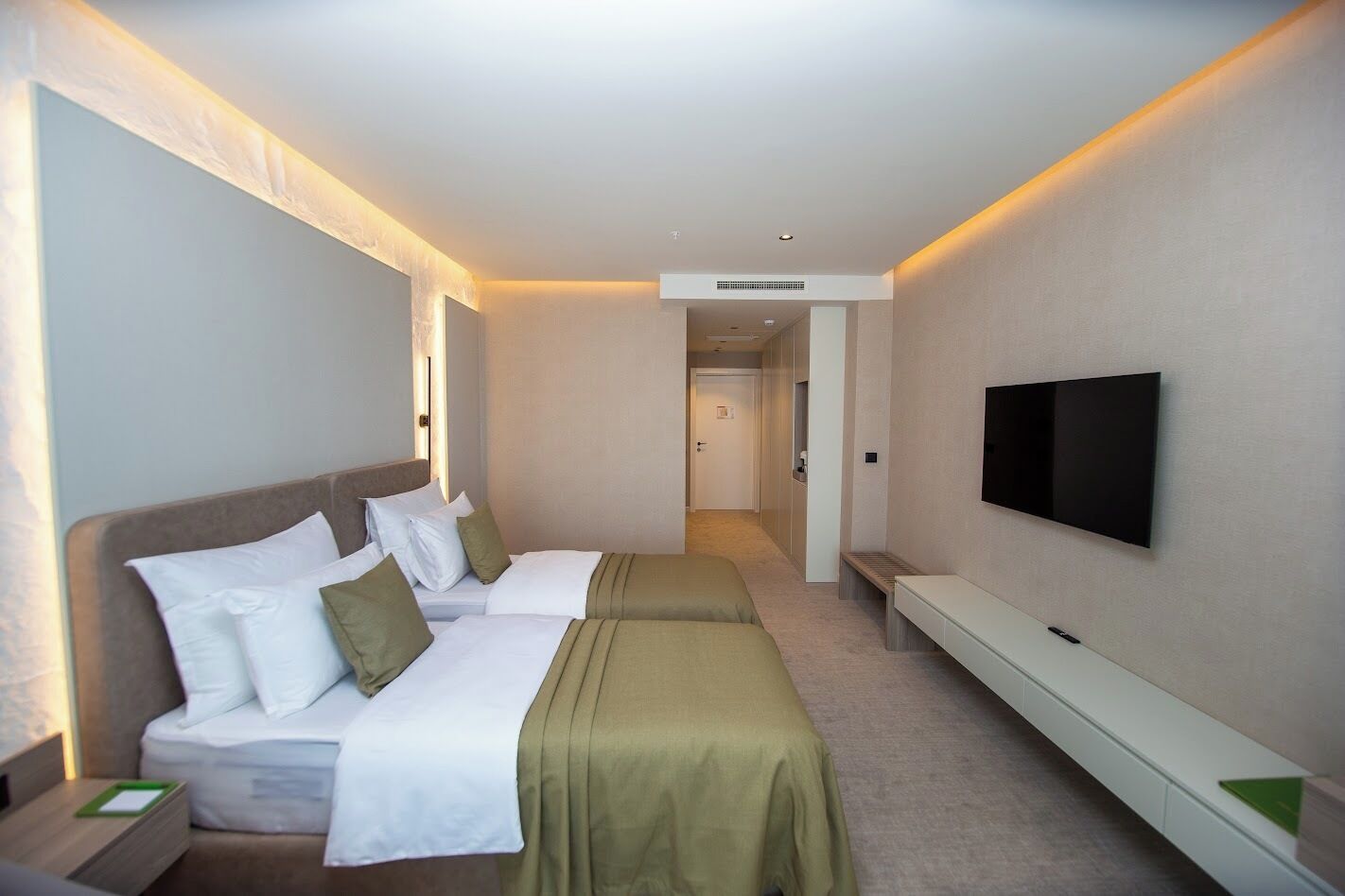 Een hotelkamer met twee bedden, een televisie en een gang naar een andere kamer.