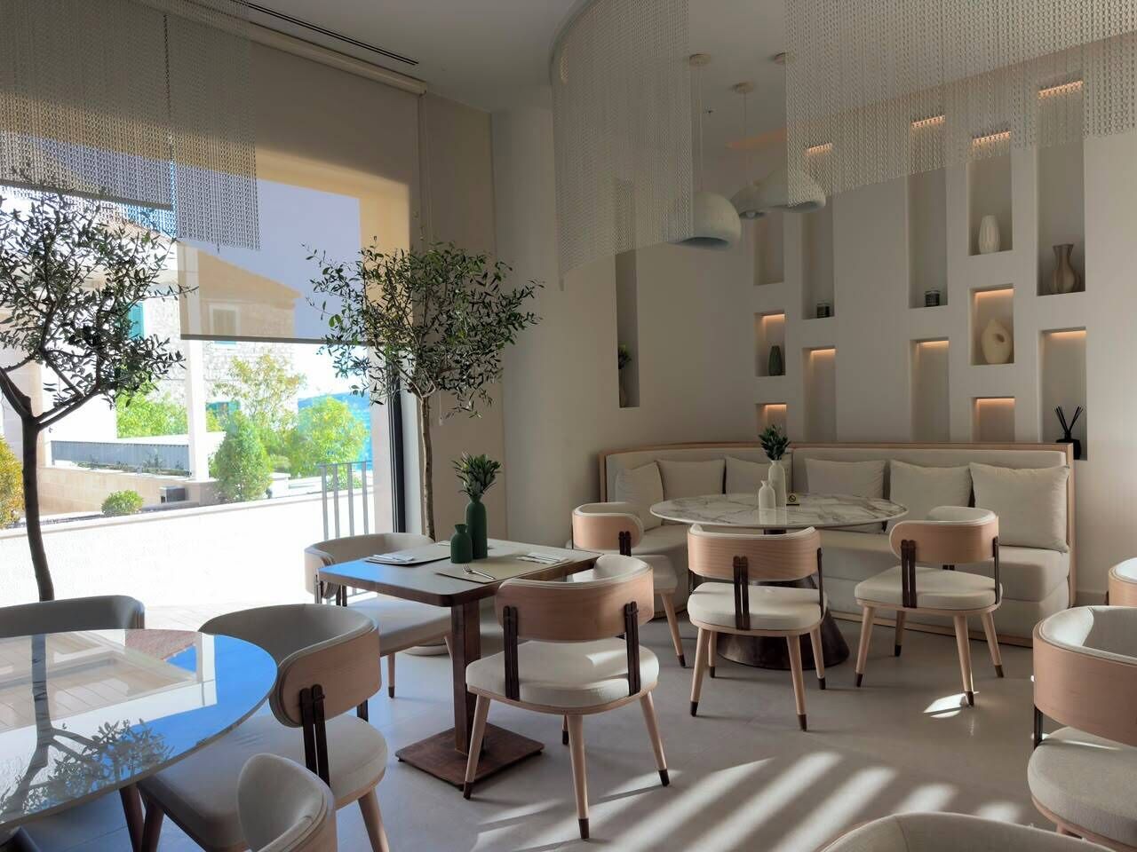 Un interior moderno con mesas redondas, sillas acolchadas y una zona de estar con sofá y sillones.