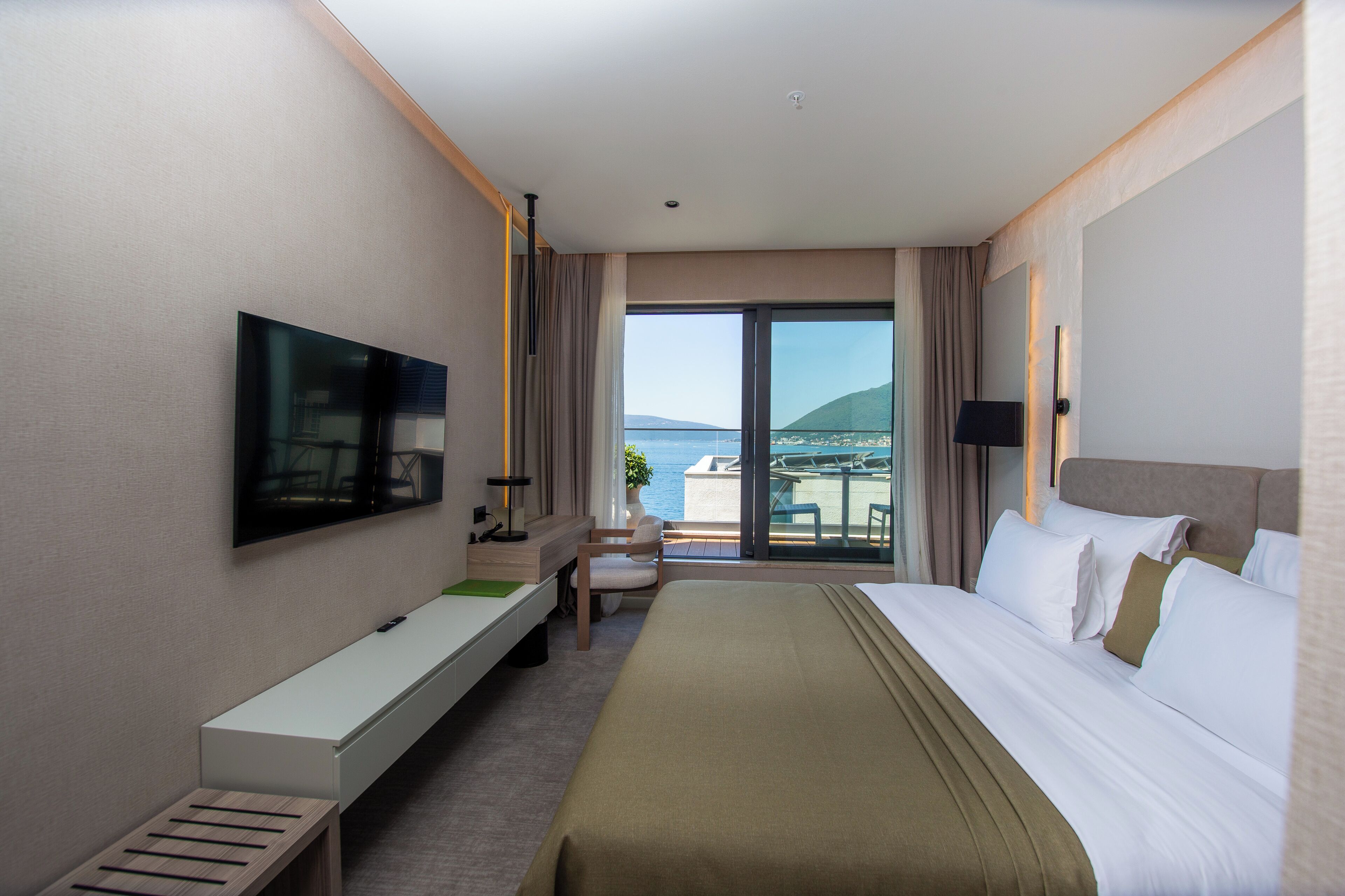 Ein Hotelzimmer mit Bett, Fernseher, Schreibtisch und einem Balkon mit Blick.