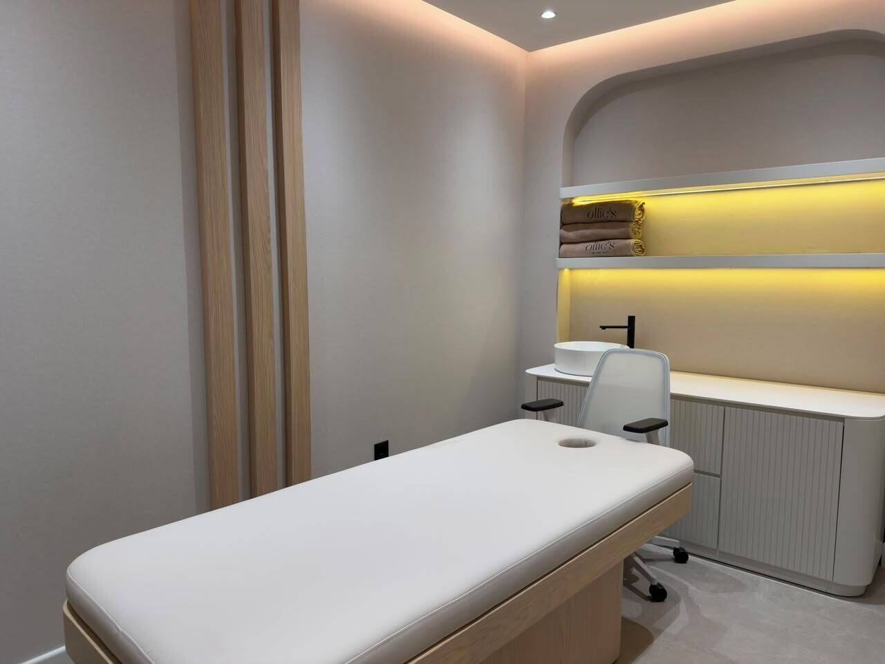 A medical examination room with a treatment bed, a desk, and a shelf with books.
