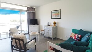 A room with a bed, a TV, a small table, a chair, and a window with a view. - Air-conditioned apartment, parking, sea view - 6 guests (Le Grau-du-Roi)