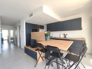 A modern kitchen with dark cabinets, a wooden dining table, and black chairs. - T3 apartment, AC & sea view - 6 guests (La Grande-Motte)
