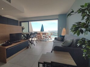 A modern living room with a sofa, a dining table, and a TV. - T3 apartment, AC & sea view - 6 guests (La Grande-Motte)