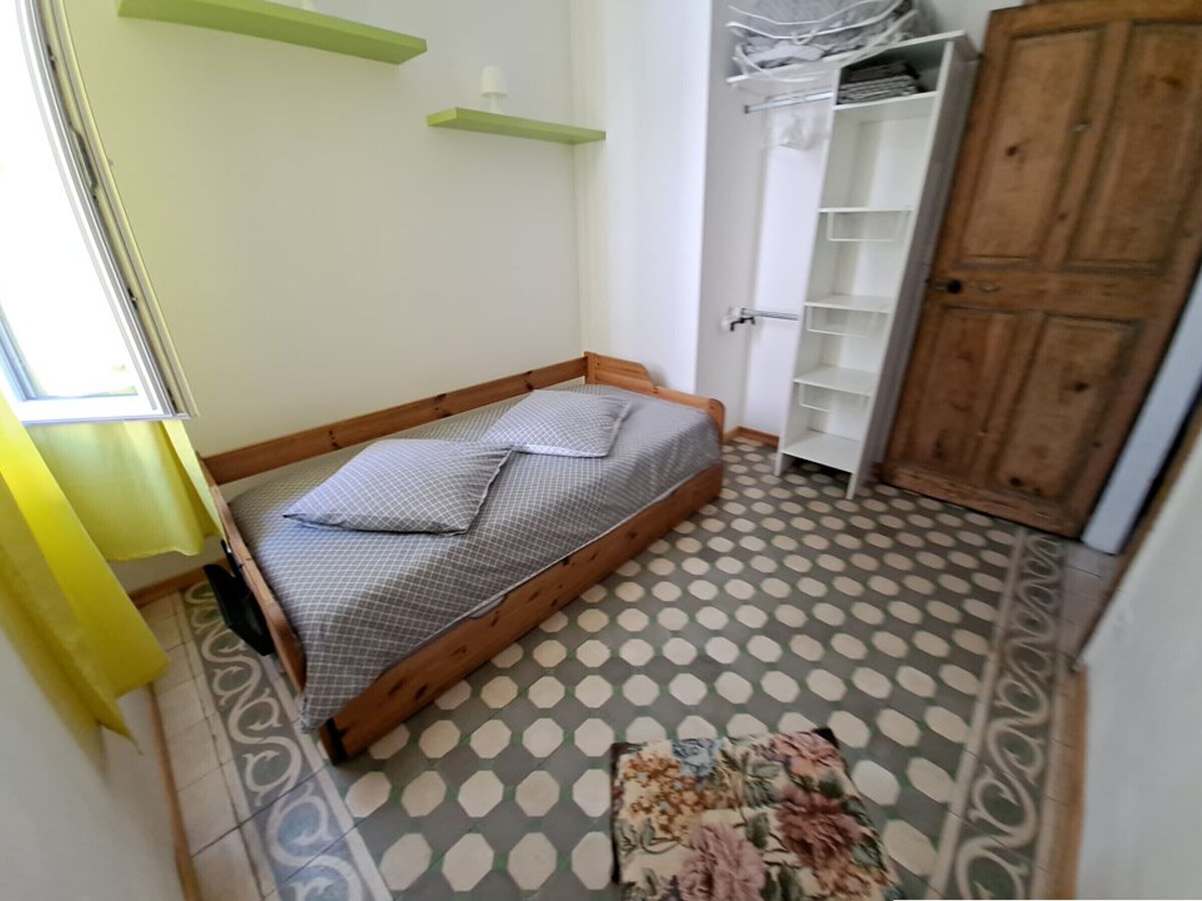A small bedroom with a single bed, a wardrobe, and a patterned floor.
