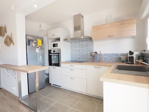 A modern kitchen with white cabinetry, a stainless steel range hood, a microwave, and an oven. - Apartment with AC and parking - 6 guests, steps from the beach (Le Grau-du-Roi)