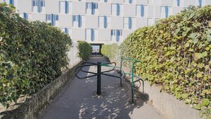 Un camino conduce a un edificio con un diseño arquitectónico moderno, con un patrón geométrico de ventanas y una entrada bordeada de setos.