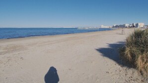 Una playa con cielo despejado, mar tranquilo y edificios a lo lejos.