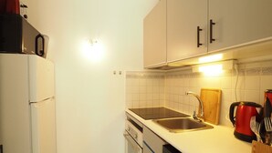Een compacte keuken met witte kastjes, een roestvrijstalen spoelbak, een rode waterkoker en een vaatwasser.
