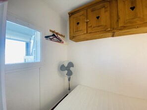 A bedroom with a window, a fan, and wooden cabinets. - Studio cabin near beach - 5 guests (La Grande-Motte)