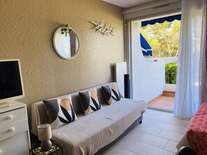 A bedroom with a sofa, a TV, a lamp, a mirror, and a sliding glass door to an outdoor area. - Studio at Boucanet, parking - 4 guests (Le Grau-du-Roi)
