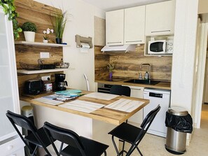 A modern kitchen with wooden accents, a microwave, a coffee maker, and a trash can. - Studio at Boucanet, parking - 4 guests (Le Grau-du-Roi)