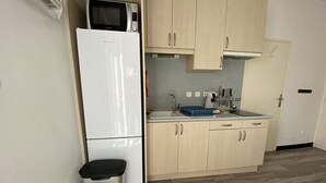 Pieni, käytännöllinen keittiö, jossa on valkoinen jääkaappi, mikroaaltouuni, pesuallas ja puiset kaapit.