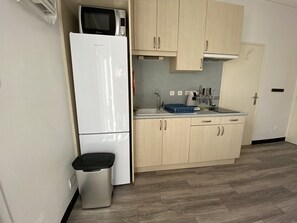 A compact kitchen with a white refrigerator, a microwave, a sink, and wooden cabinets. - Lovely flat AC city center - 6 guests (Le Grau-du-Roi)